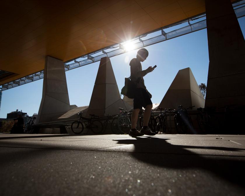 Person walking under Gates Hall overhang, sun setting behind them