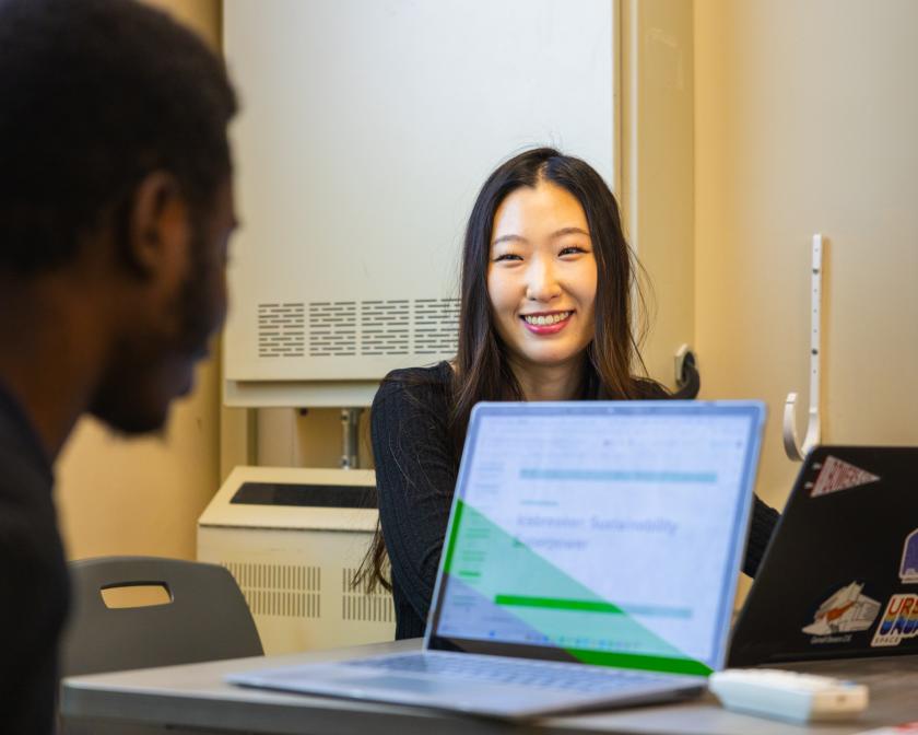 A woman and man sit together on their laptops. The woman is smiling.
